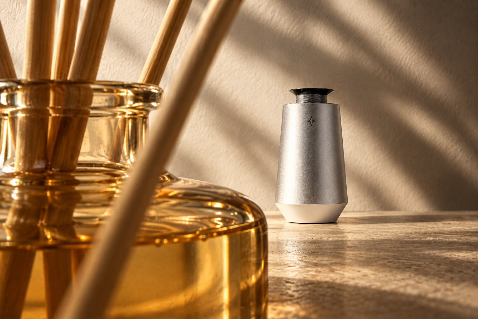 Close-up of an amber glass reed bottle, looking past the reeds toward silver Vessel 01 in warm side light.