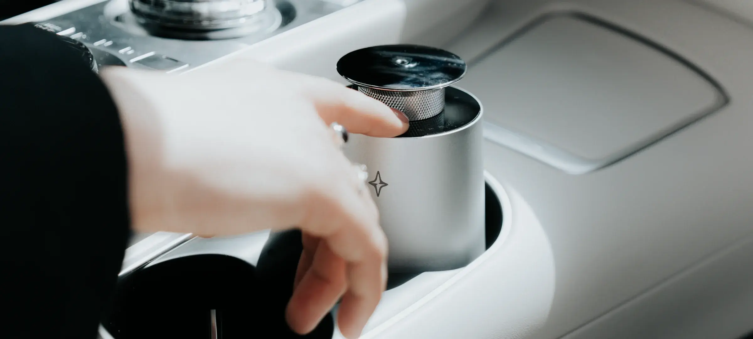 A hand holding the silver Vessel 01 diffuser in a car cup holder.